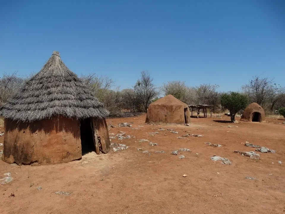 Un villaggio culturale tradizionale in Namibia mostra strutture abitative in terra battuta sotto un cielo azzurro.