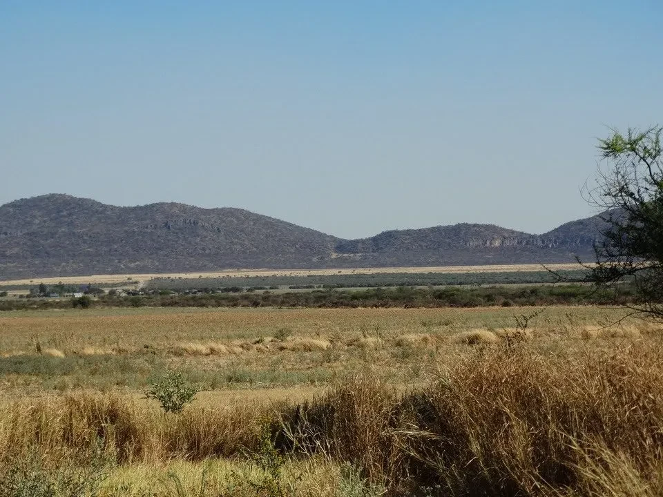 Paesaggio arido di colline ondulate e vegetazione secca sotto un cielo limpido.