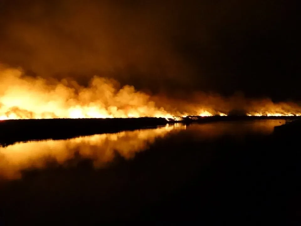 Un vasto fuoco arde su un paesaggio scuro con riflessi sull'acqua. Un vasto fuoco arde su un paesaggio scuro con riflessi sull'acqua.