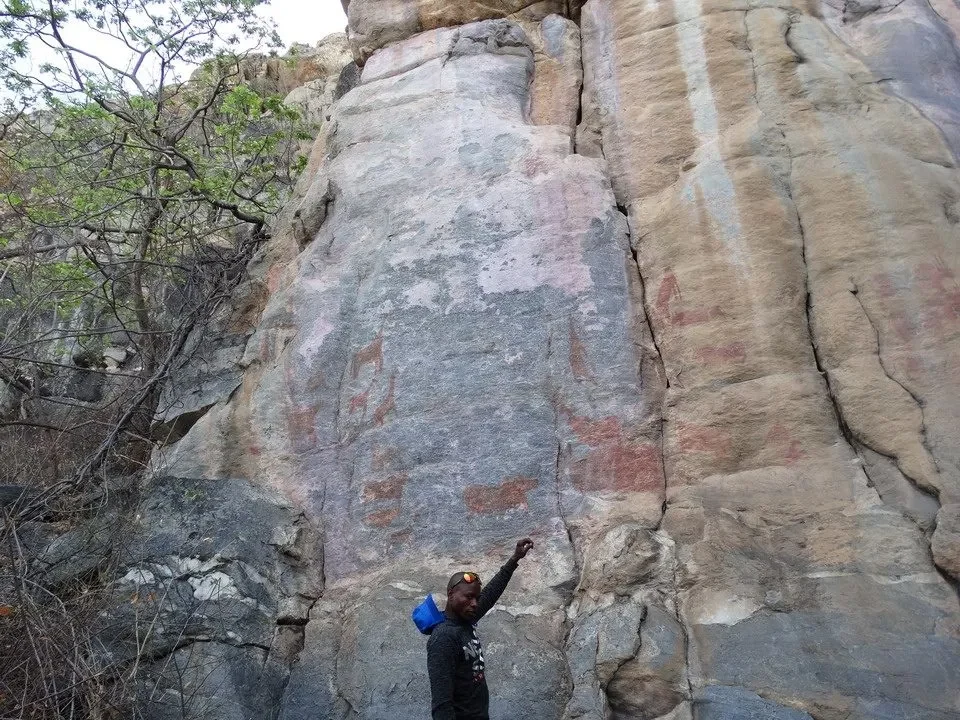 Un uomo si staglia davanti a una grande formazione rocciosa con tracce di arte rupestre in Namibia.