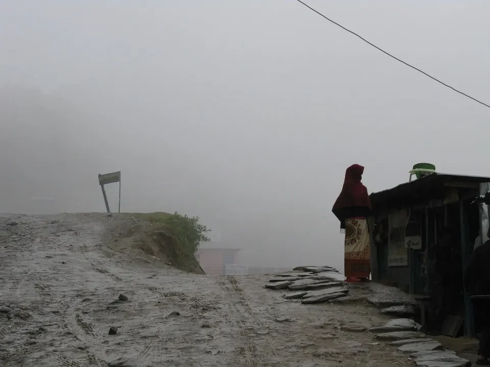 Sentiero montano innevato e una struttura in legno in una nebbia fitta.