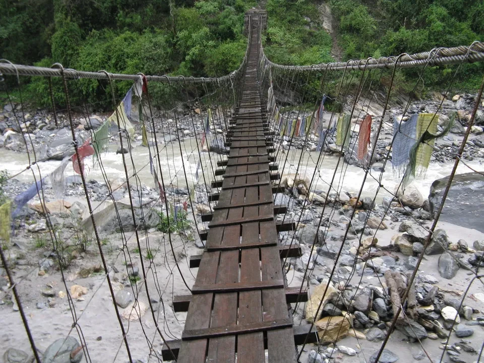 Un ponte sospeso di legno attraversa un fiume rochoso in un paesaggio montano.