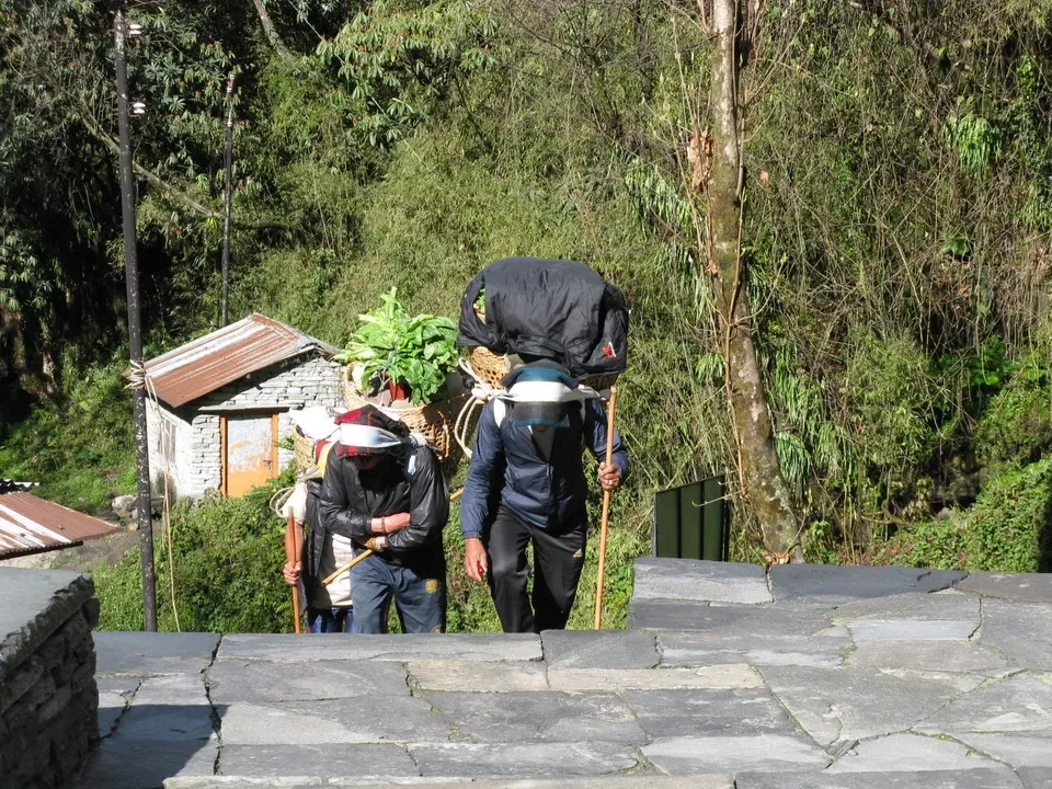Due uomini trasportano pesanti borse su una terrazza in montagna.