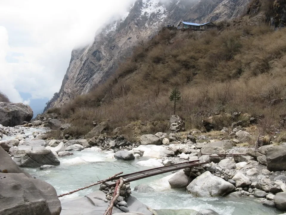 Un hotel si trova su un pendio roccioso con un fiume che scorre in primo piano.
