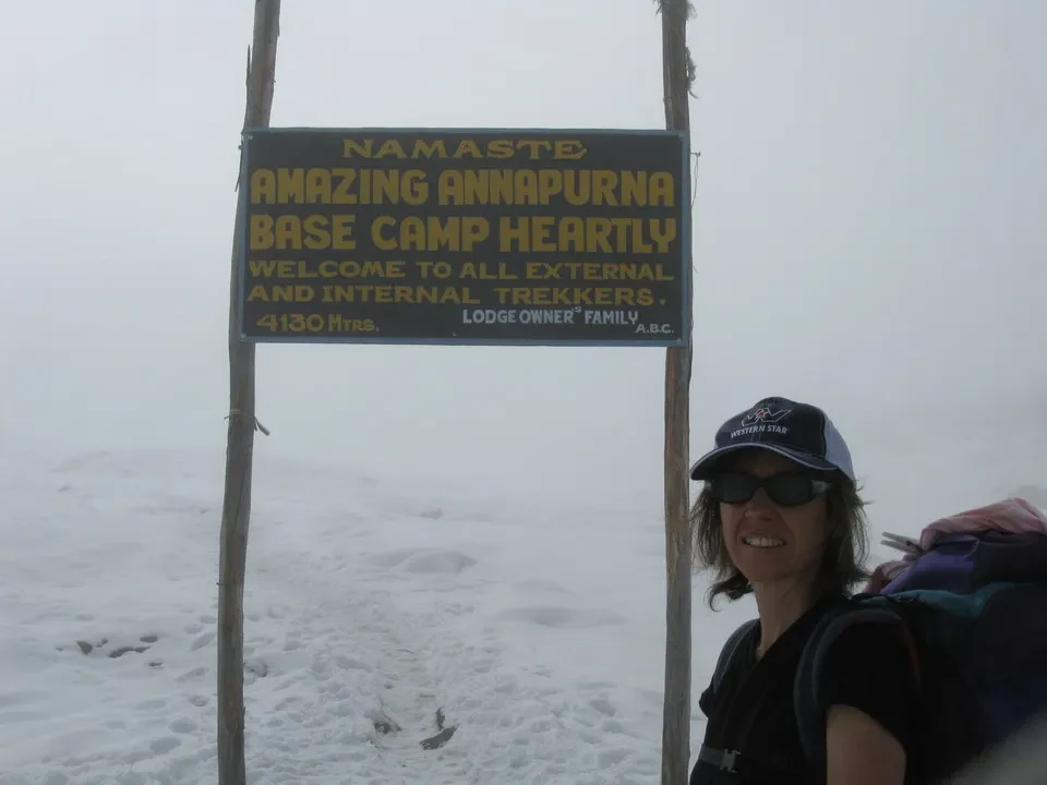 Una donna sorride davanti a un cartello del campo base in un ambiente innevato.
