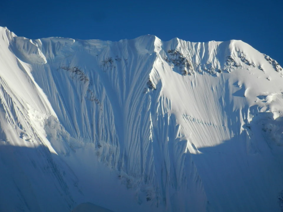 Vaste montagne innevate con ombre profonde sotto il cielo blu.