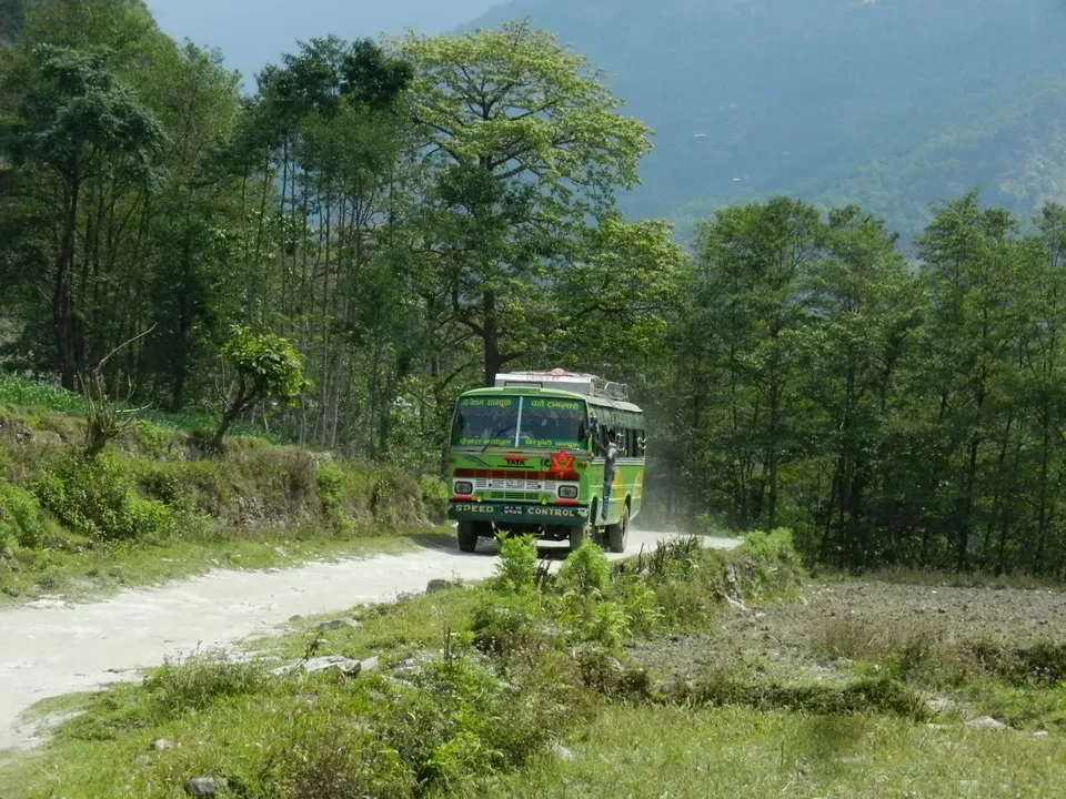 Un autobus percorre una strada sterrata attraverso un paesaggio montano in Nepal o Tibet.