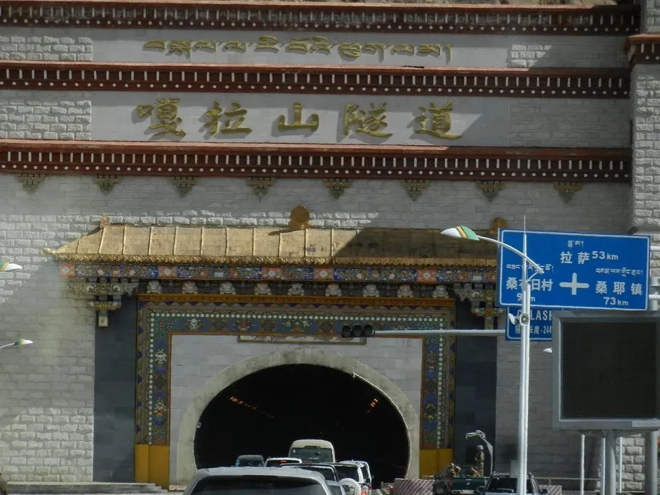 Ingresso monumentale con iscrizioni tibetane lungo una strada montuosa.