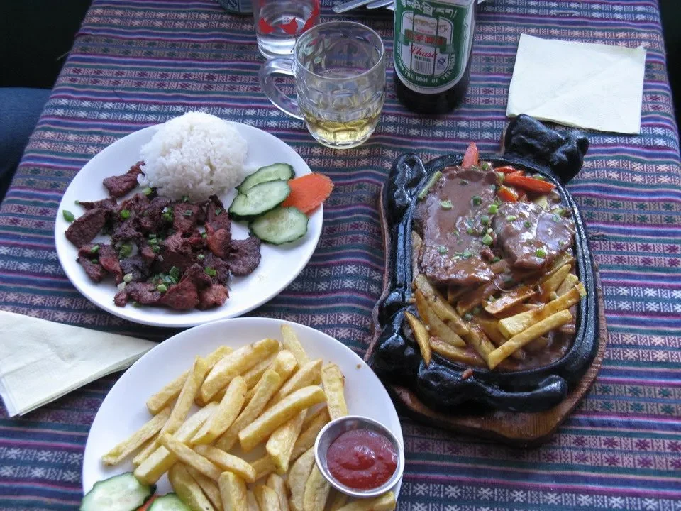 Un pasto tradizionale con carne, riso e patatine fritte è disposto su un tavolo.