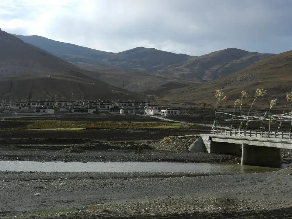 Paesaggio montano del Shegar in Nepal con un piccolo insediamento e un ponte in primo piano.