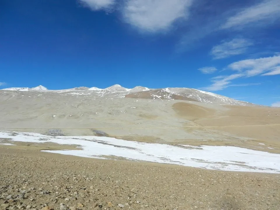 Paesaggio montano arido con cime innevate sotto un cielo azzurro e nuvoloso.