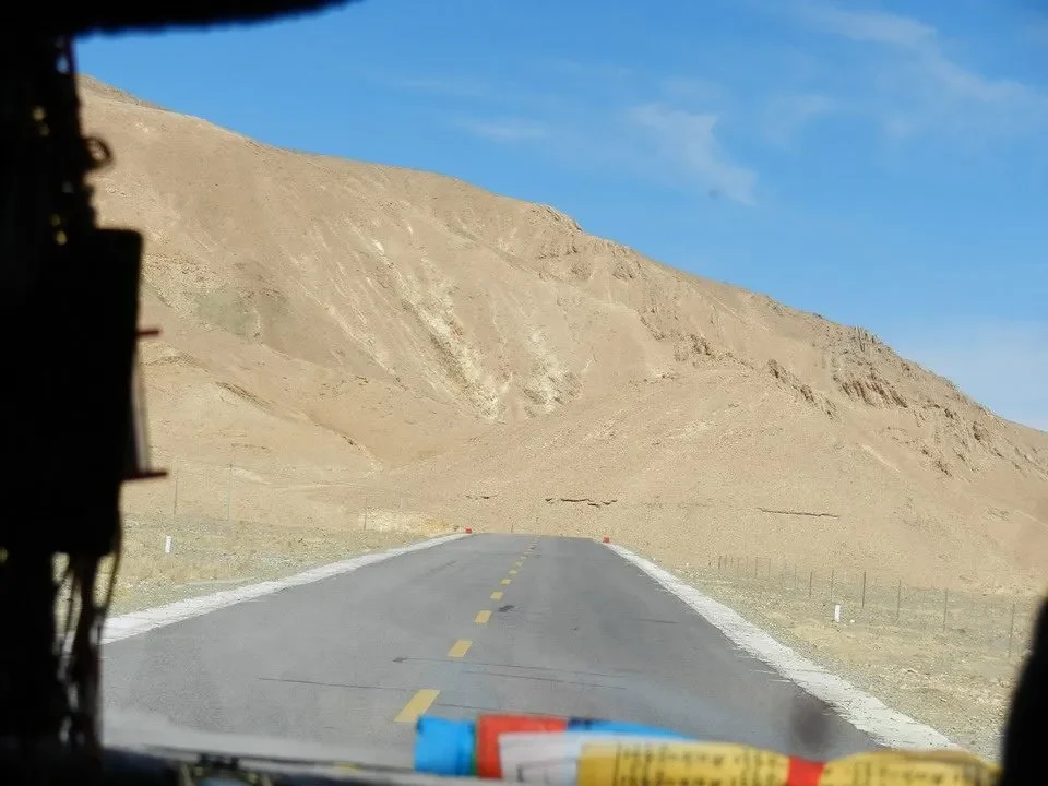 Una strada asfaltata attraversa un paesaggio montano arido in Nepal o Tibet.