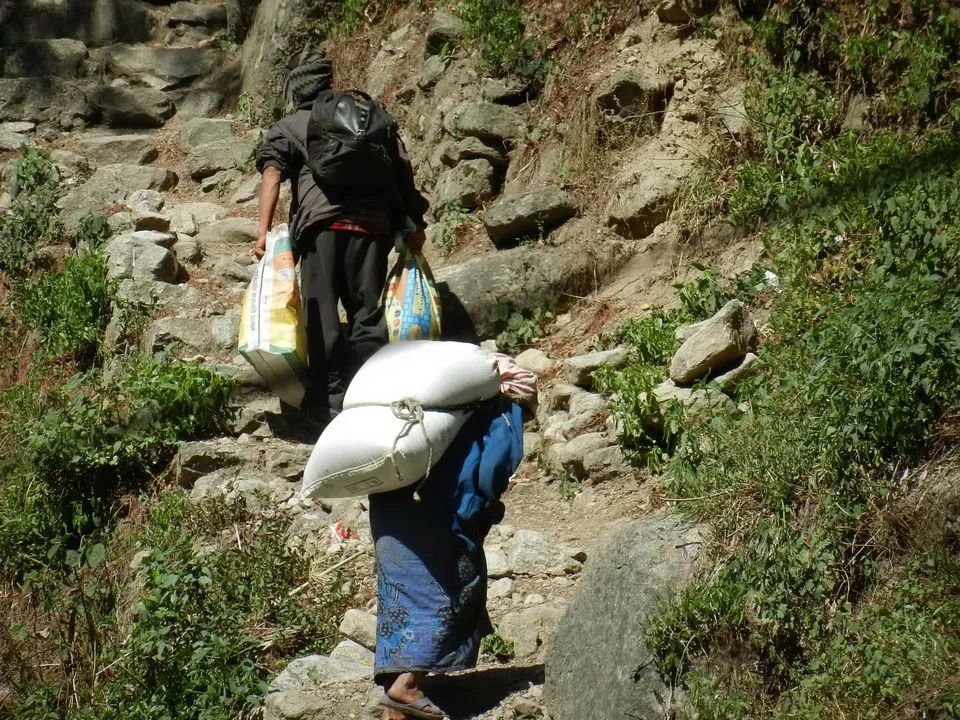 Un viaggiatore trasporta pesanti carichi lungo un sentiero montano in Nepal o Tibet.