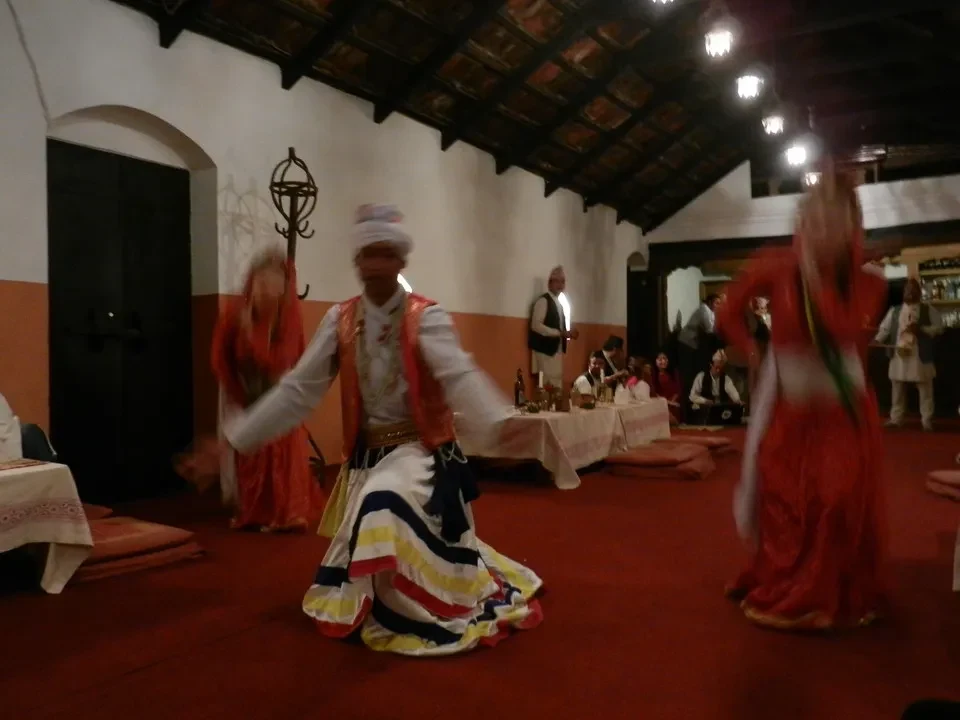 Danza tradizionale in un interno rustico con costumi colorati.