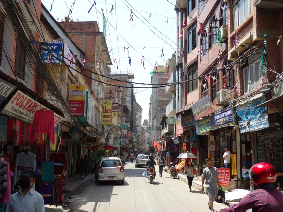 Una strada trafficata a Kathmandu con negozi lungo i lati.