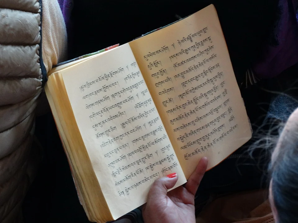 Una mano tiene aperto un libro con testo tibetano in un contesto di viaggio.