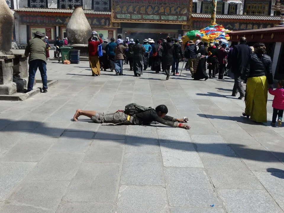 Persone passeggiano in una piazza aperta con elementi architettonici tibetani.