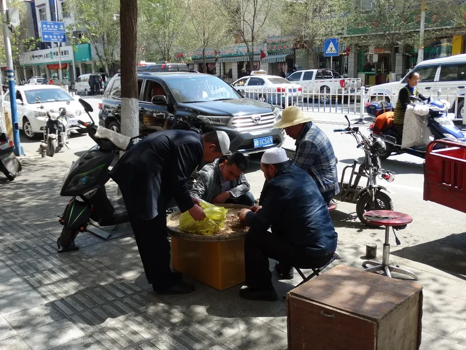 Persone si siedono a terra in un'area urbana con veicoli parcheggiati.