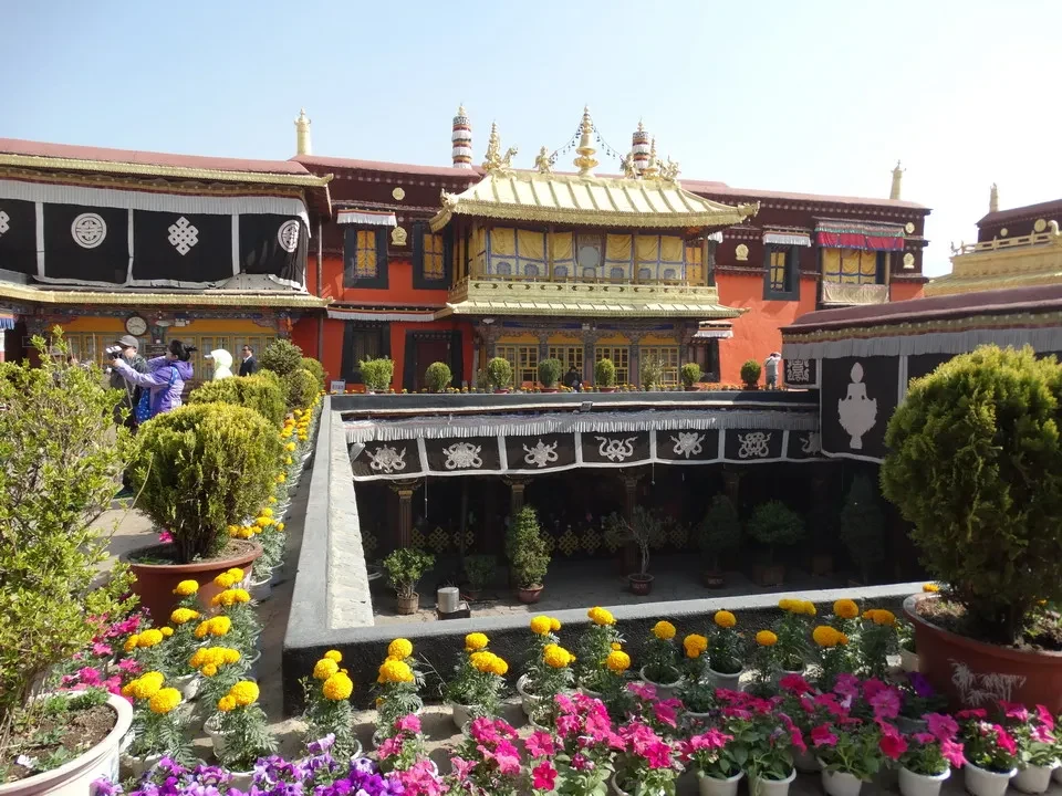 Vista di un monastero tibetano circondato da giardini fioriti e vegetazione curata.