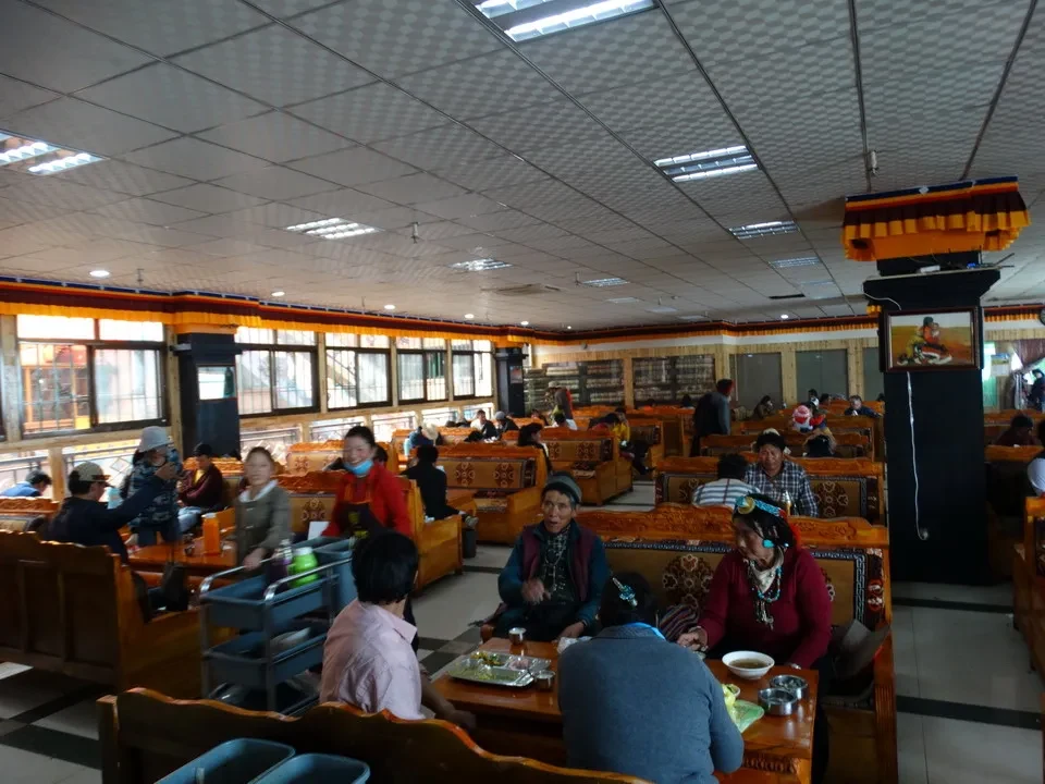 Interno di un monastero tibetano con persone sedute in una sala comune.