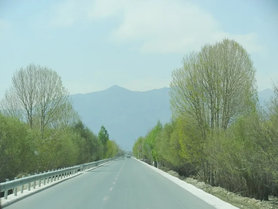 Una strada asfaltata costeggia montagne verdi nel paesaggio tibetano.