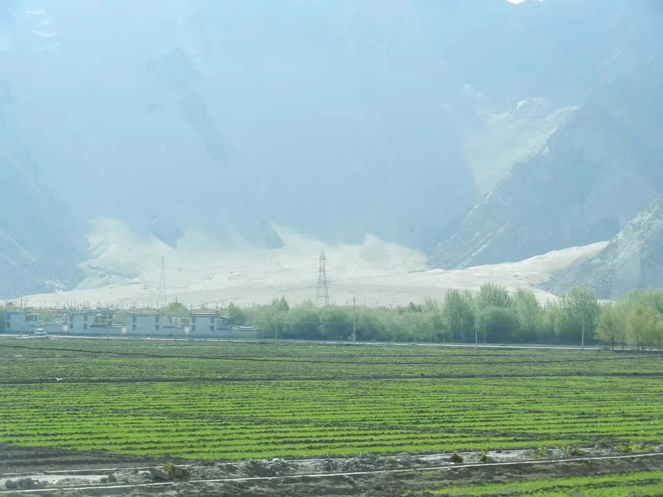 Paesaggio montano del Tibet con campi verdi in primo piano.