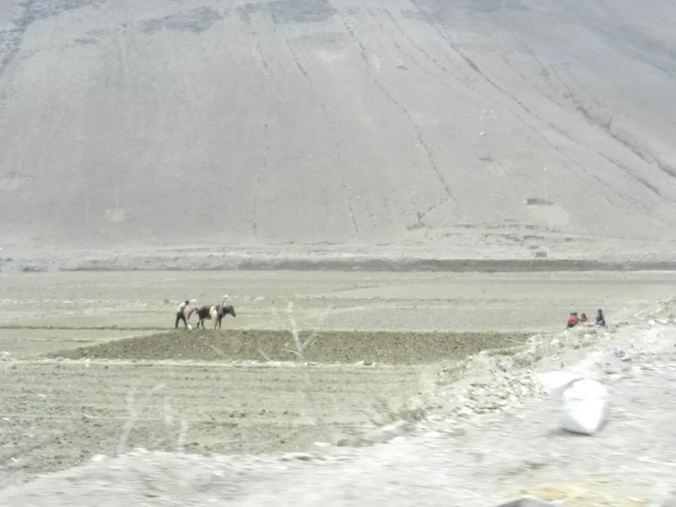 Paesaggio montano vasto con terreno arido e alcune figure in lontananza.