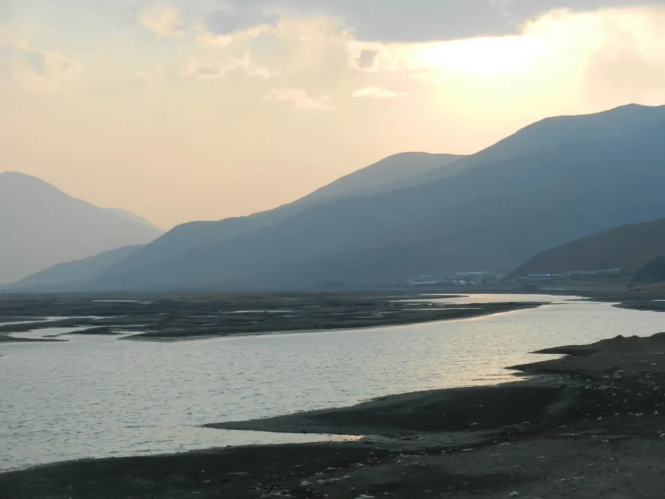 Paesaggio montano vasto con un fiume che riflette la luce al tramonto in Tibet.
