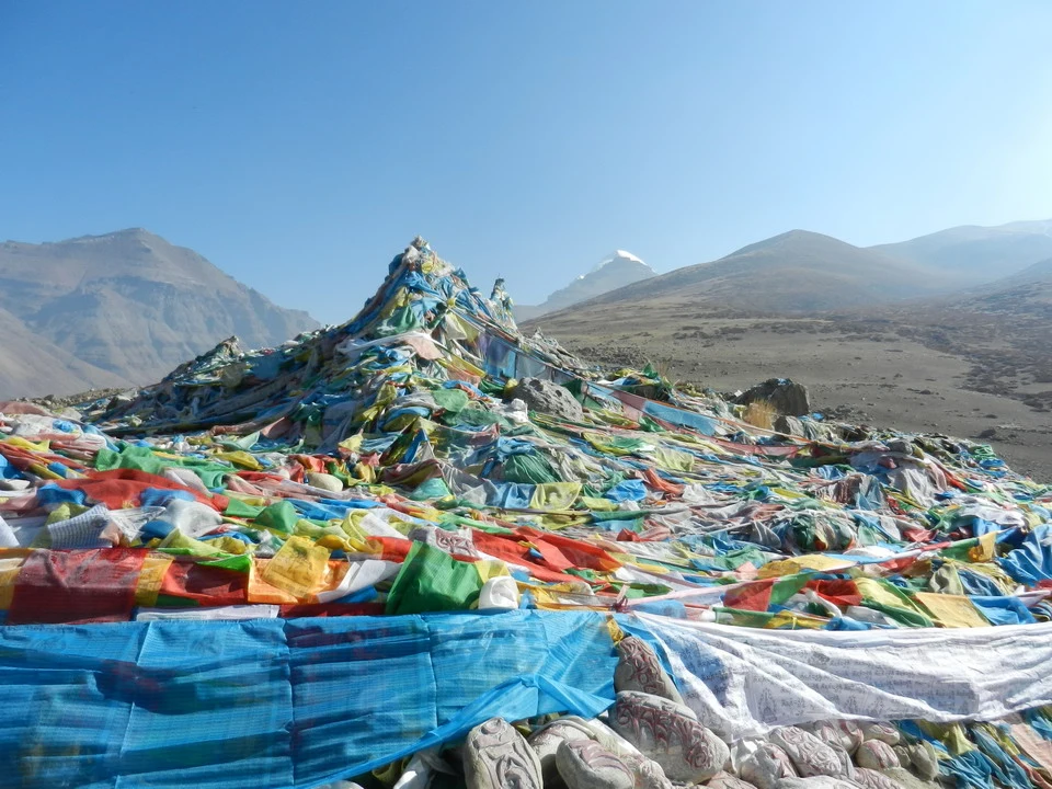 Un tappeto colorato si estende su un paesaggio montano con il Kailash visibile in lontananza.