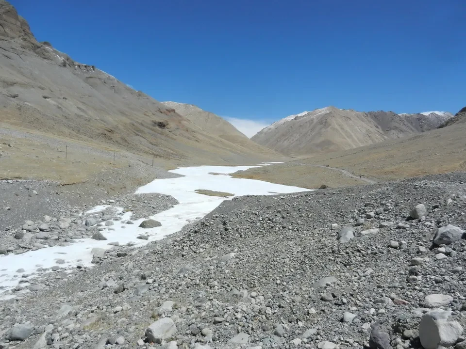 Paesaggio montano arido con un letto di fiume roccioso e innevato.