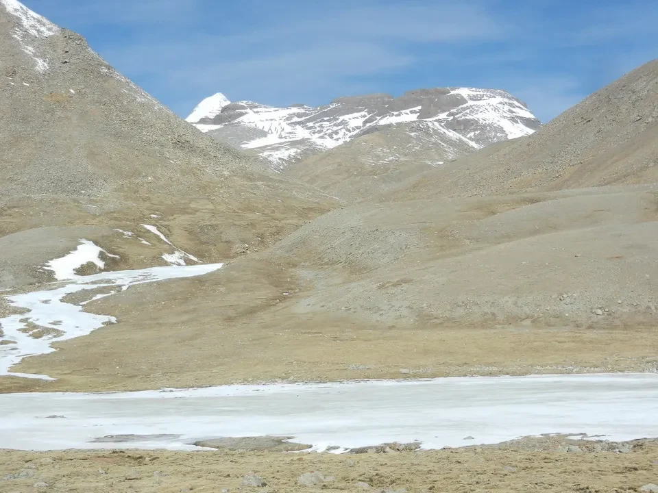 Paesaggio montano arido con montagne innevate sullo sfondo.