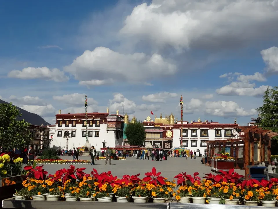 Piazza di Barkhor a Lhasa, Tibet, con edifici tradizionali e fiori colorati in primo piano.