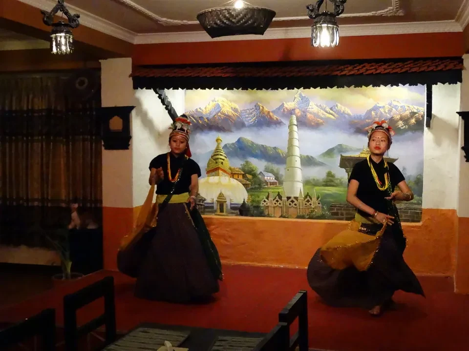 Due danzatori in costume tradizionale tibetano all'interno di una sala decorata.