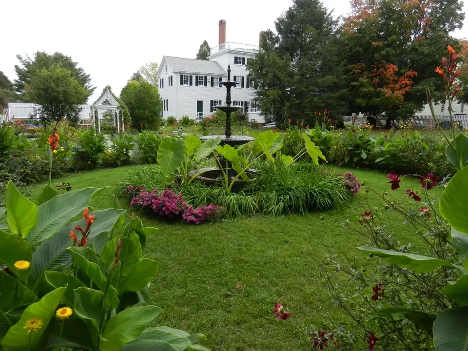 Giardino verde con una casa bianca in stile New England sullo sfondo.