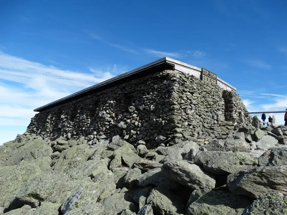 Una casa in pietra si staglia su un paesaggio roccioso sotto il cielo blu.