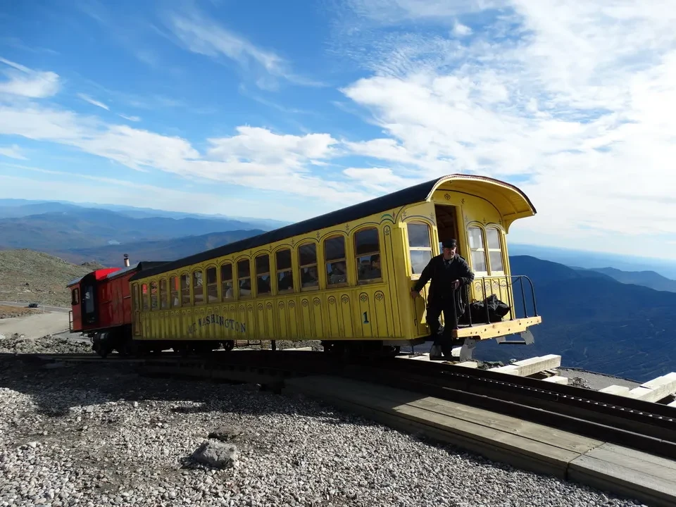 Un treno giallo attraversa un paesaggio vasto in New England.
