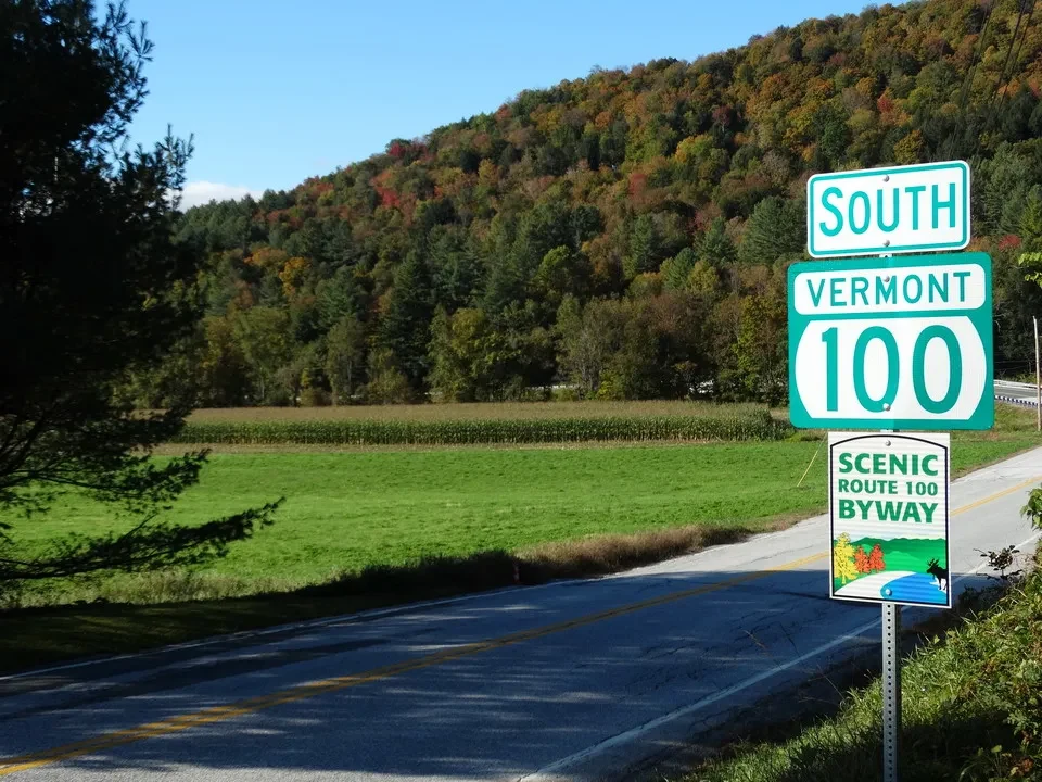 Una strada panoramica attraversa una collina autunnale in New England con segnali stradali.