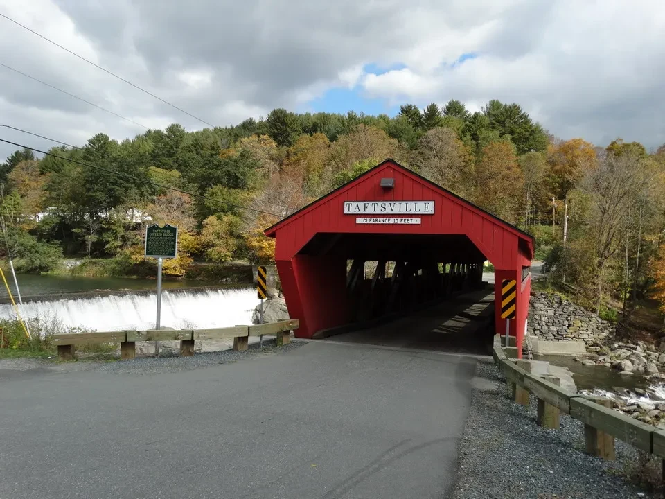 Una struttura rossa sopraelevata attraversa un piccolo corso d'acqua in una zona boscosa della New England.