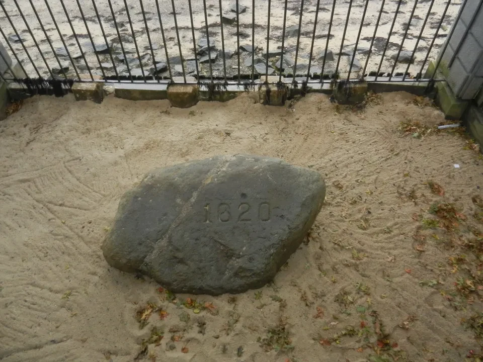 Una grande pietra con una data incisa giace sulla sabbia vicino all'acqua.