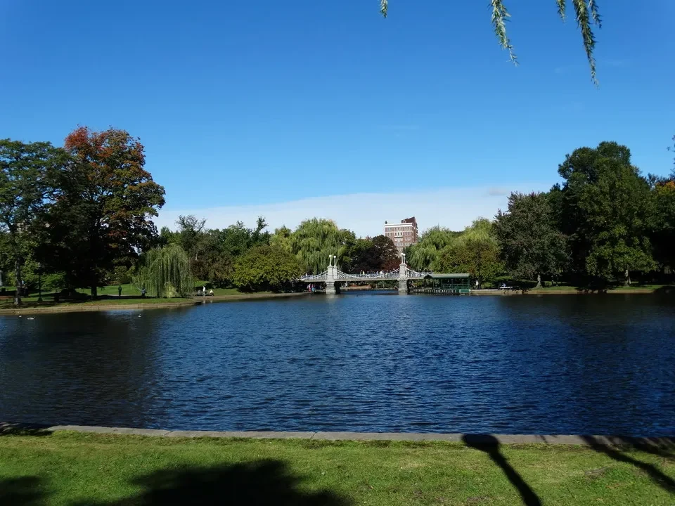 Un giardino pubblico con un ponte attraversa uno specchio d'acqua in una giornata di sole nel New England.