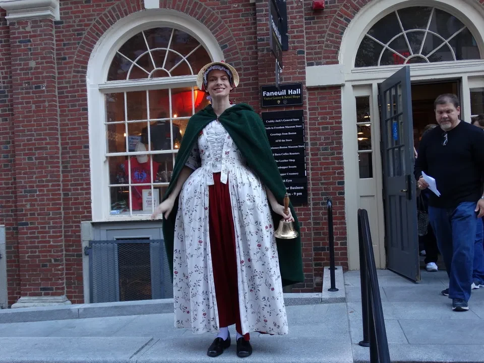 Una donna indossa un abito lungo e una veste verde davanti a un edificio storico.