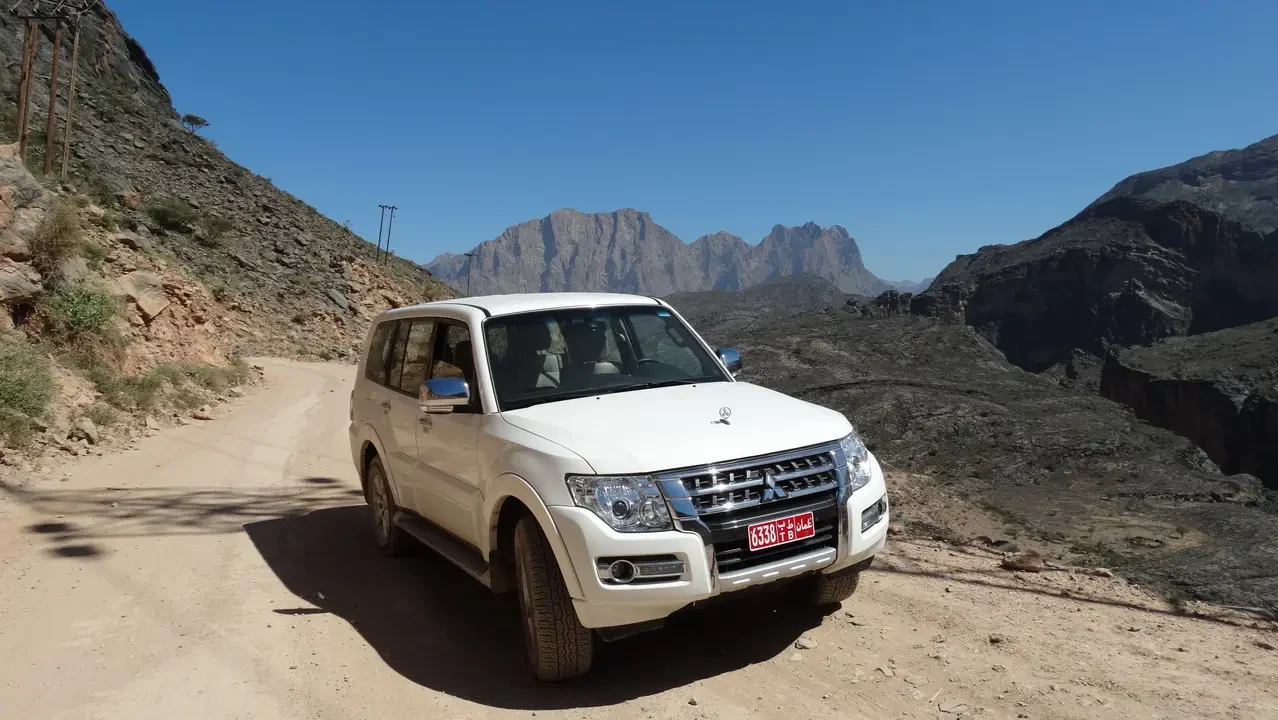 Un veicolo bianco percorre una strada sterrata attraverso un paesaggio montuoso in Oman.