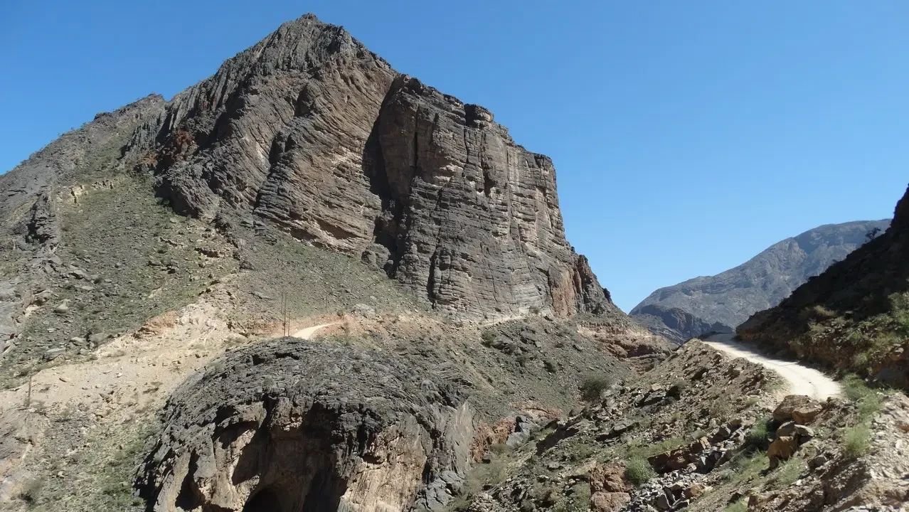Paesaggio montano arido con una strada sterrata che attraversa un canyon in Oman.