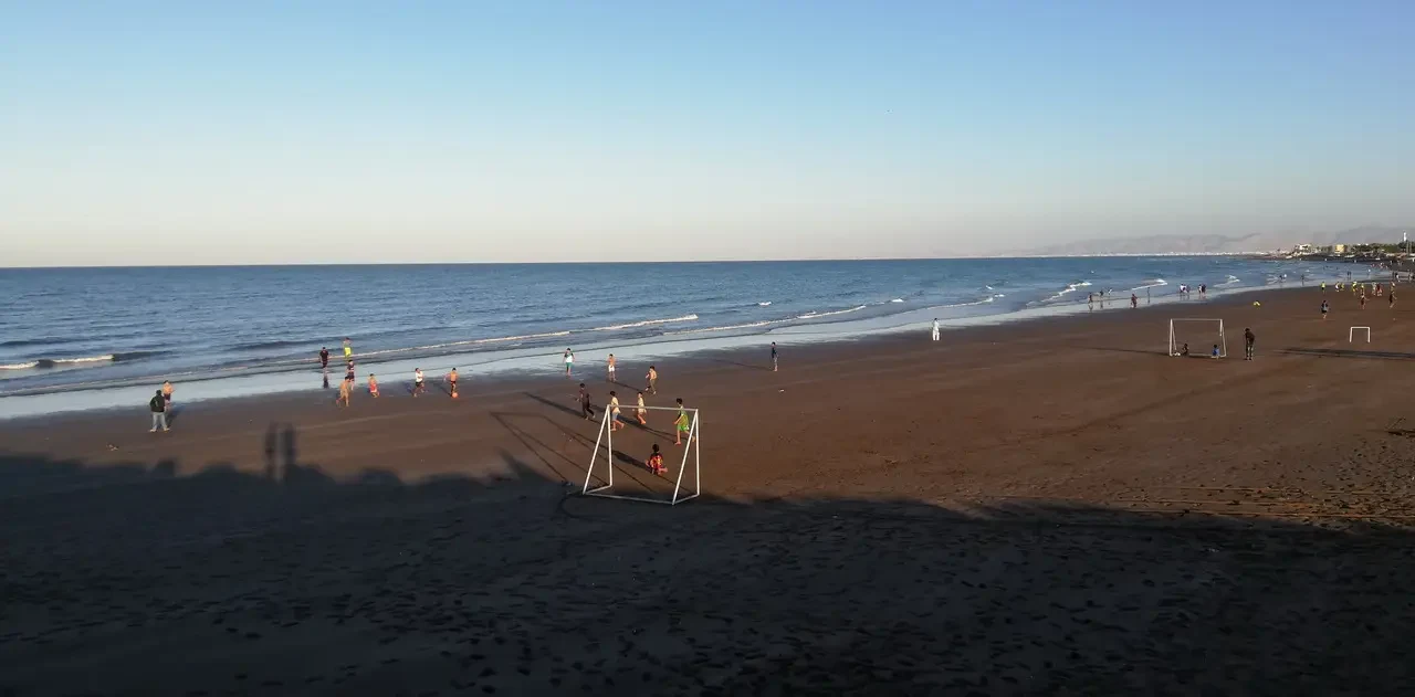 Una spiaggia ampia con persone che giocano a calcio vicino all'oceano.