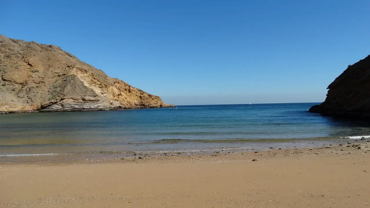 Spiaggia sabbiosa con coste rocciose e acqua turchese sotto un cielo limpido.