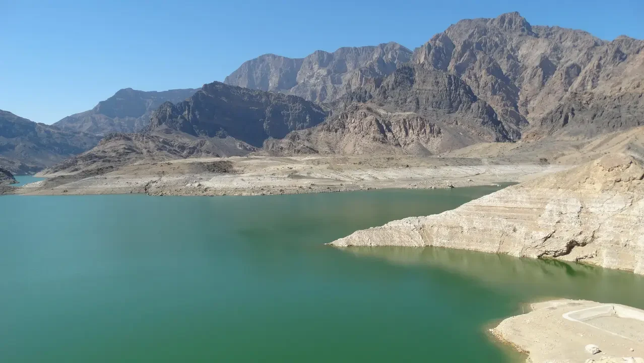 Un lago turchese si estende tra le montagne aride dell'Oman e degli Emirati Arabi Uniti.