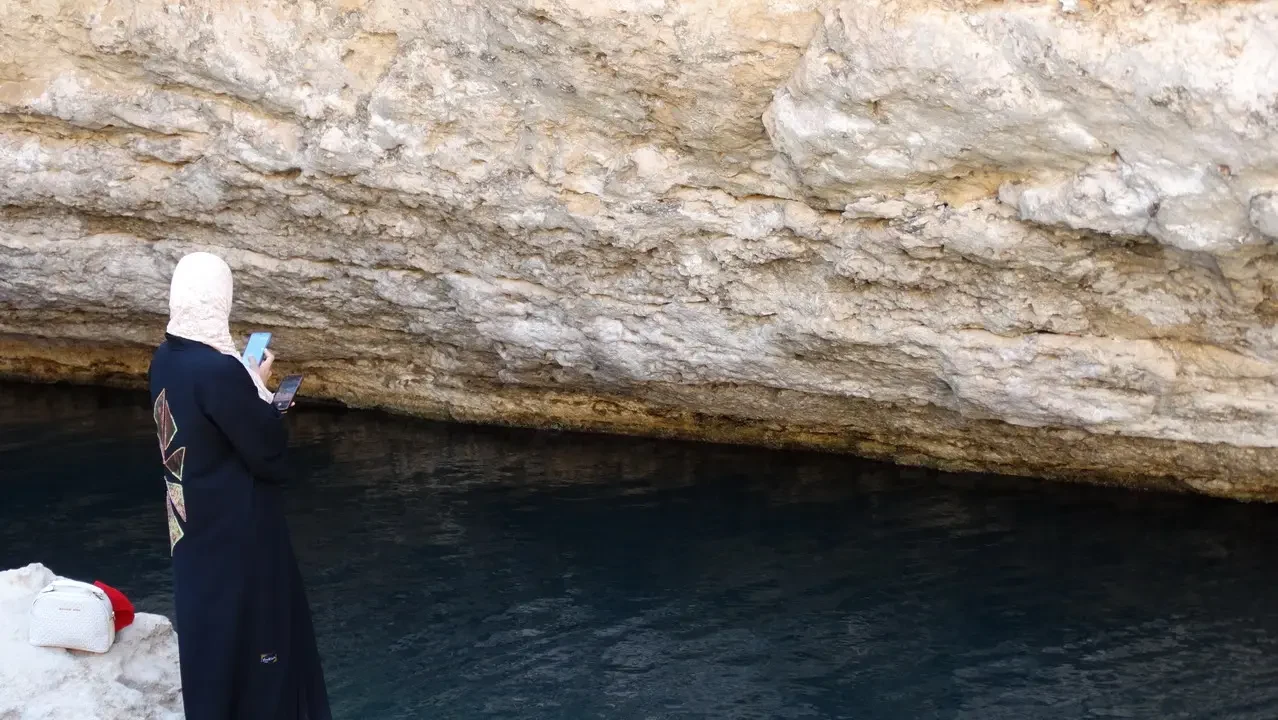 Una persona guarda una formazione rocciosa costiera con il mare in primo piano.