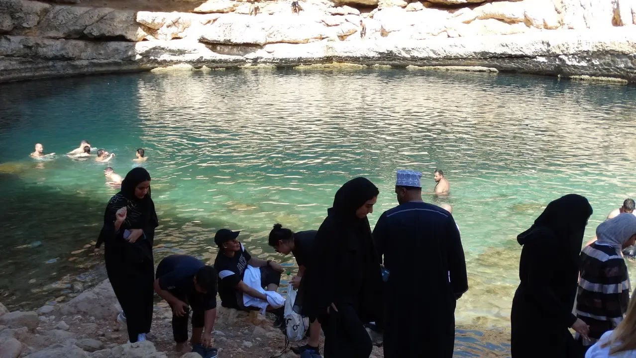 Un gruppo di persone si trova in una pozza d'acqua cristallina tra rocce chiare.