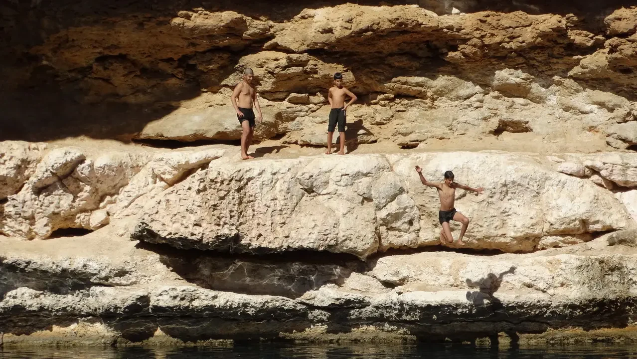 Uomini posano su rocce chiare sopra l'acqua in un paesaggio arido.