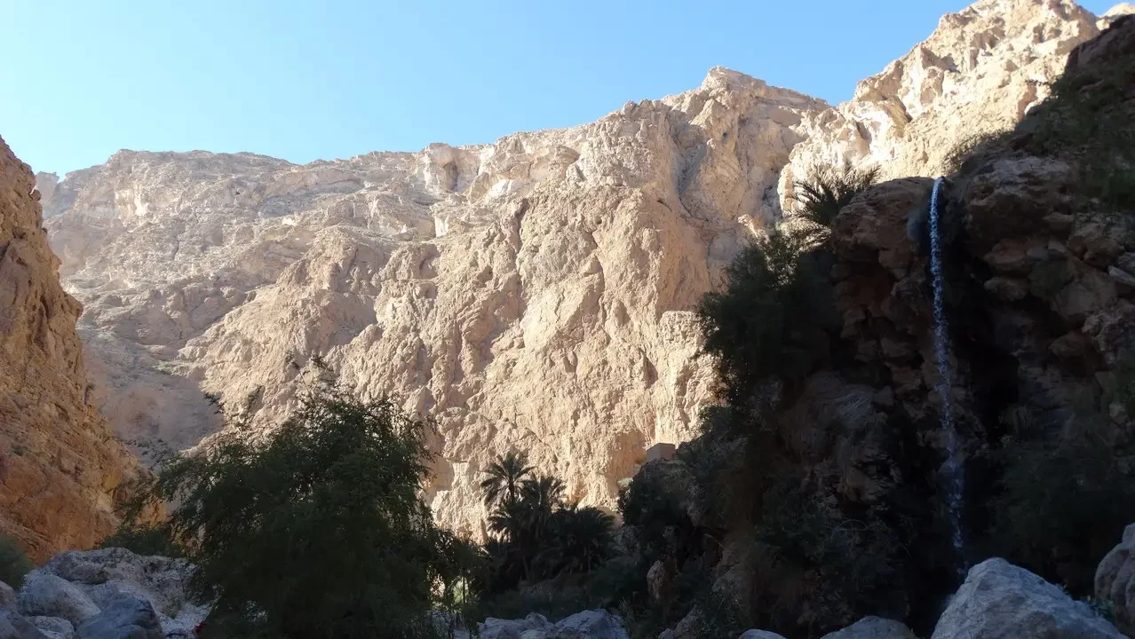Una cascata scorre lungo una gola rocciosa nel paesaggio arido dell'Oman o degli Emirati Arabi Uniti.